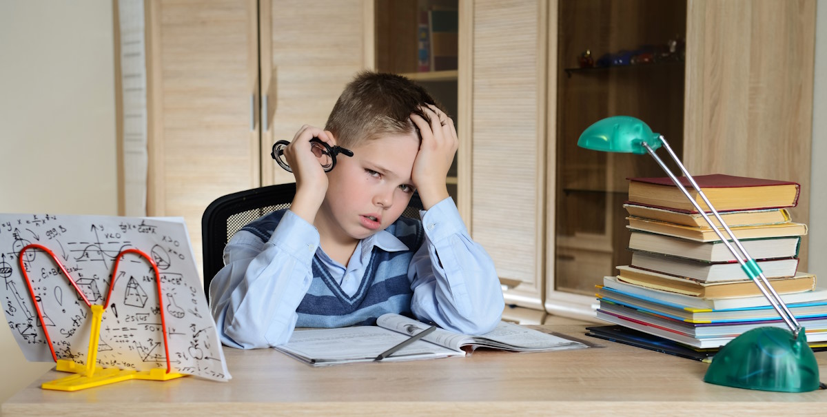 Enfant fatigué faisant ses devoirs, livres et schéma posés sur le bureau